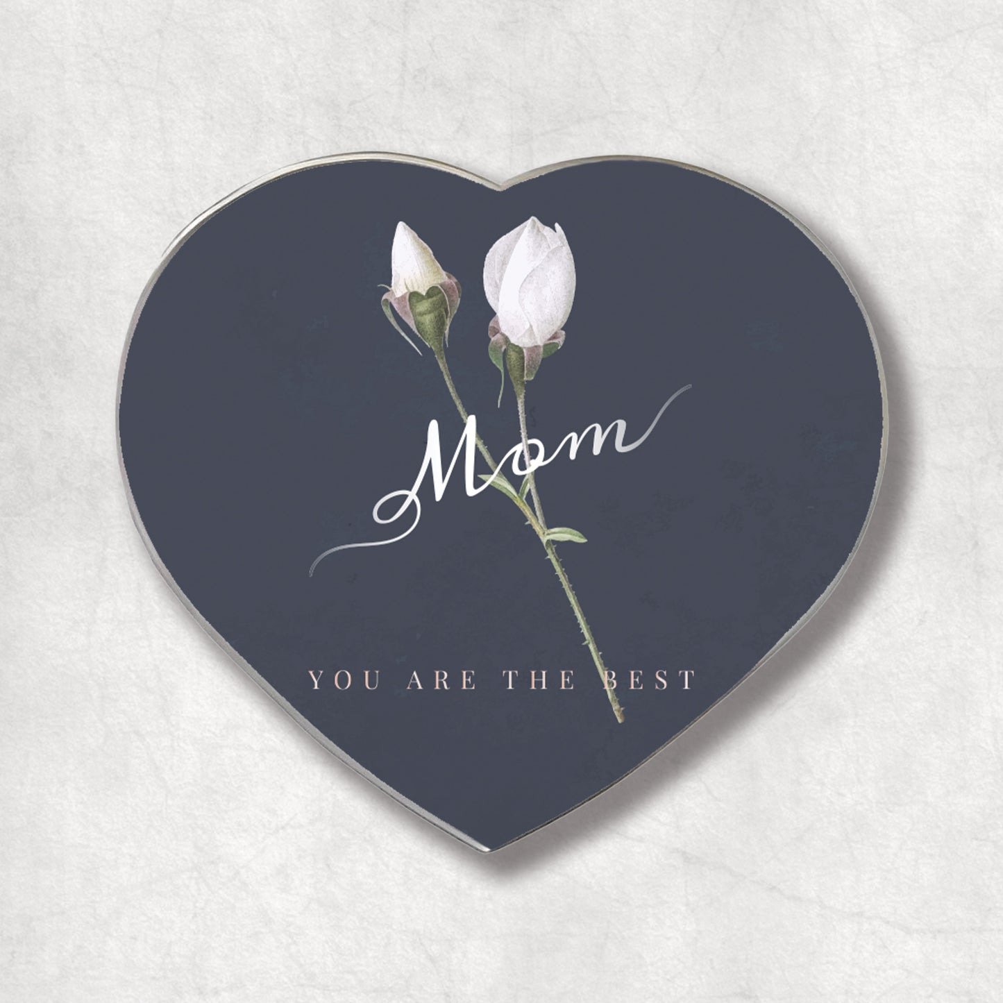 A heart-shaped metal magnet with the 'Mom YOU ARE THE BEST' text on a dark background, accompanied by an image of two white roses.