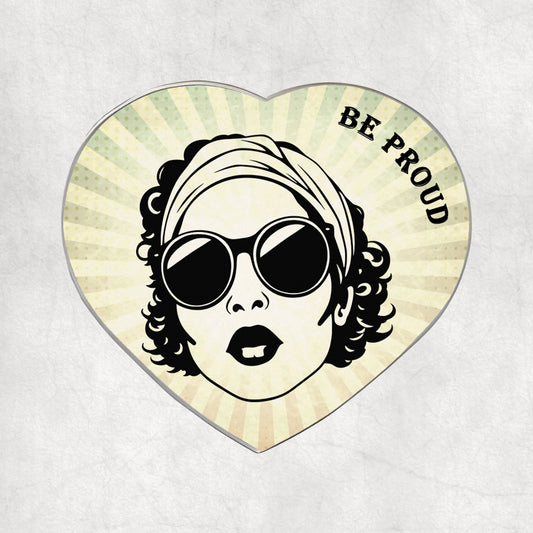 Heart-shaped metal magnet with a stylised  woman's face wearing sunglasses and a headscarf, with 'BE PROUD' text on a light vintage background.