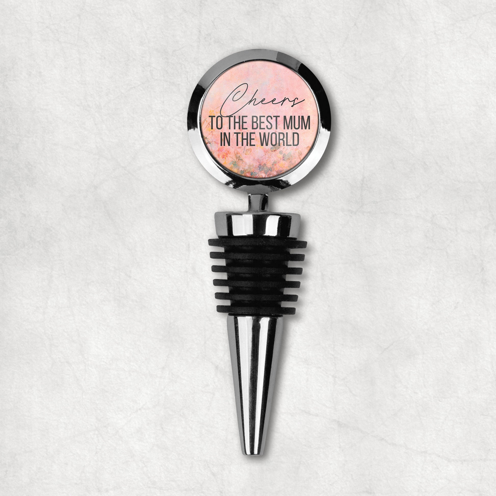 Wine stopper with a round top that has text 'Cheers to the best mum in the world' on a floral background, attached to a black rubber stopper and a metal structure.