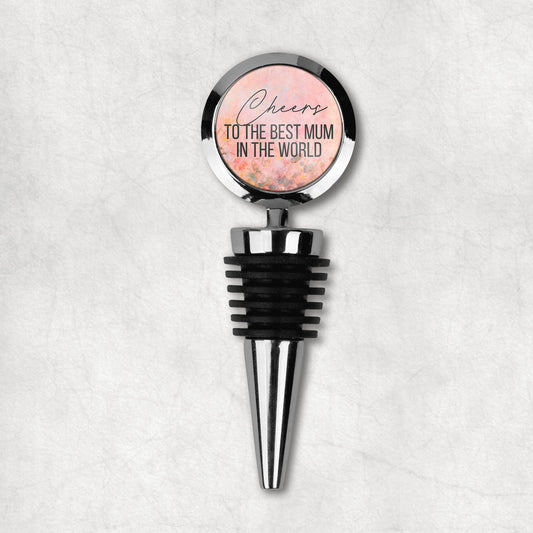 Wine stopper with a round top that has text 'Cheers to the best mum in the world' on a floral background, attached to a black rubber stopper and a metal structure.