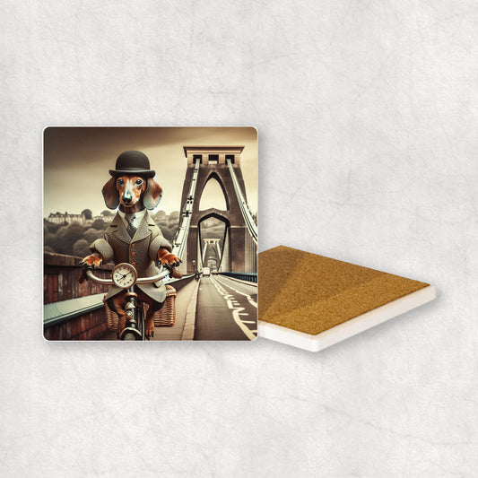 Ceramic coaster with a Dachshund dog design, dressed in a suit and a hat, riding a bike on the Clifton Suspension Bridge.