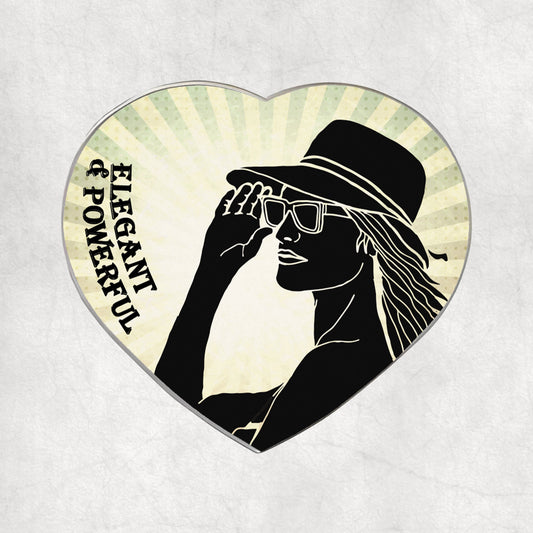 Heart-shaped metal magnet with a silhouette of a woman wearing a hat and sunglasses, and the text 'Elegant & Powerful' on a light vintage background.