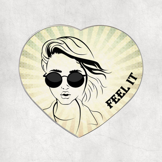 Heart-shaped metal magnet with a stylised face wearing sunglasses and 'FEEL IT' text on a light vintage background.