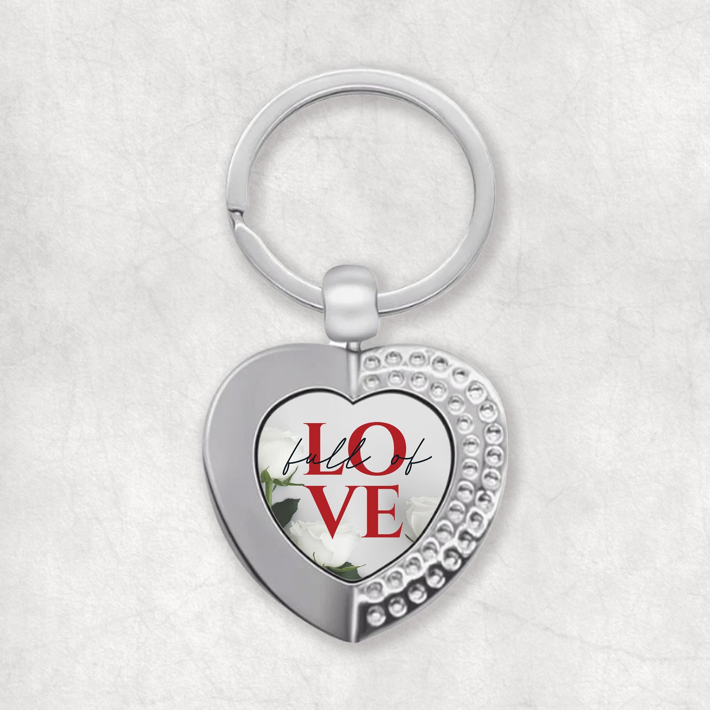 A heart-shaped keyring with the words 'Full of Love' printed on it, predominantly in silver color with red text.