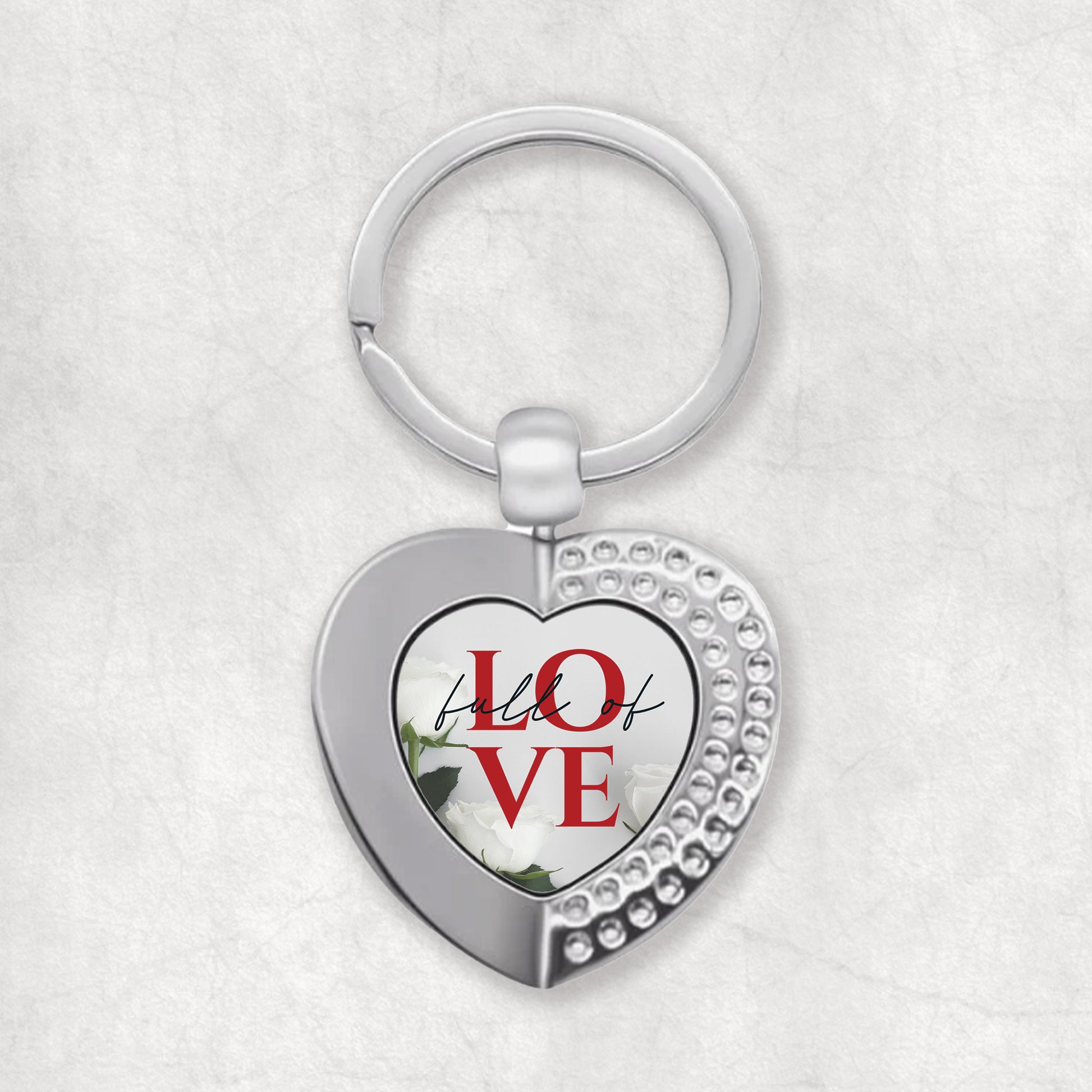 A heart-shaped keyring with the words 'Full of Love' printed on it, predominantly in silver color with red text.