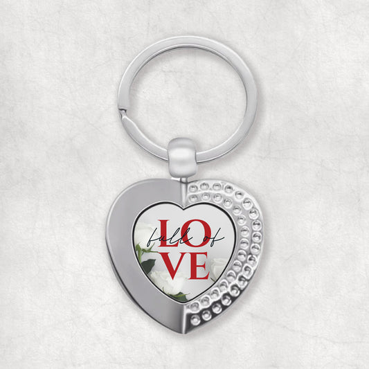 A heart-shaped keyring with the words 'Full of Love' printed on it, predominantly in silver color with red text.
