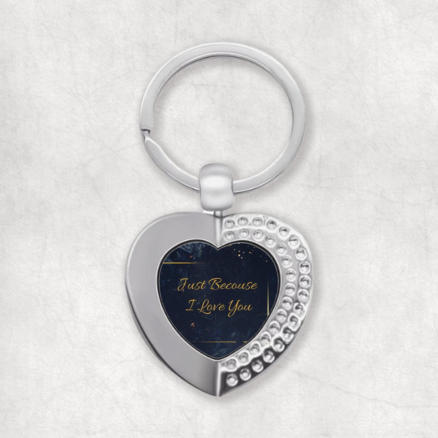 A heart-shaped keyring with the phrase 'Just Because I Love You' printed on it, predominantly in a dark color with white and gold accents.