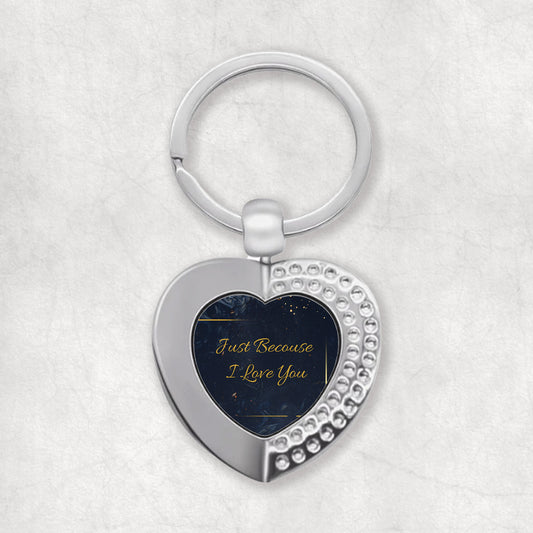 A heart-shaped keyring with the phrase 'Just Because I Love You' printed on it, predominantly in a dark color with white and gold accents.