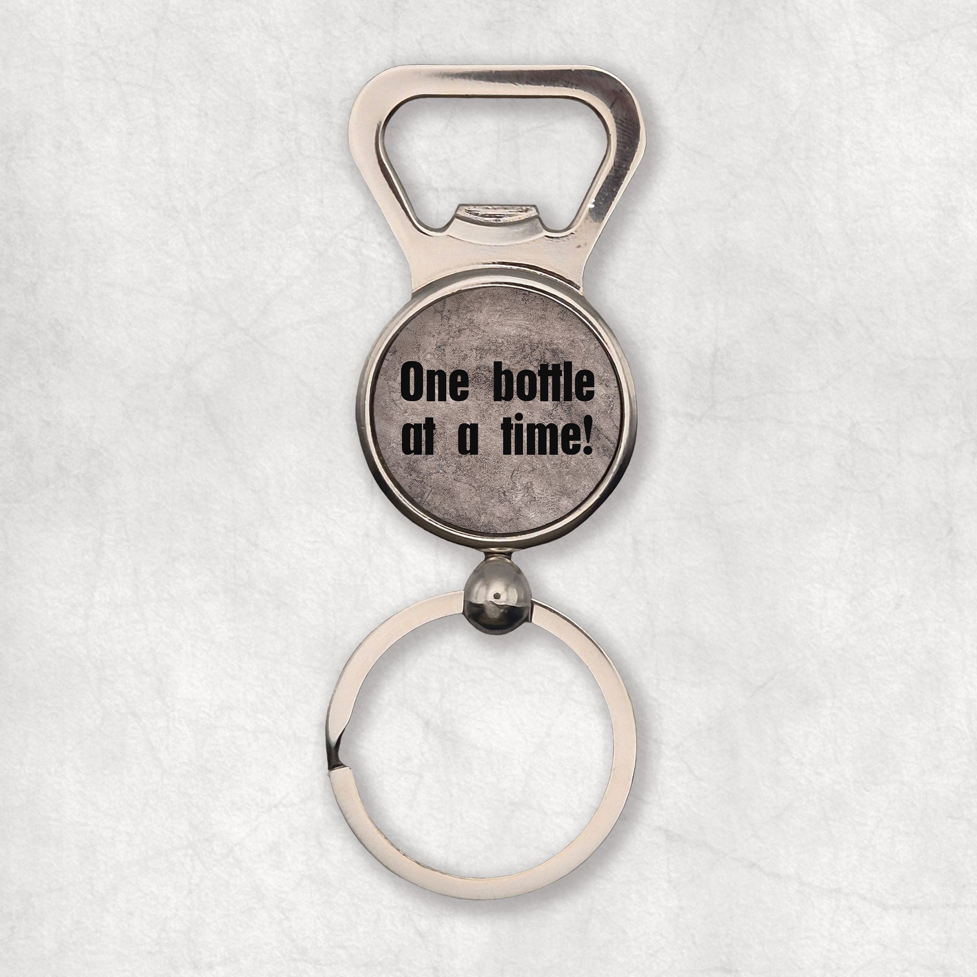 Bottle opener kayring with 'One bottle at a time' text  on a greyish background, the perfect gift for any occasion.