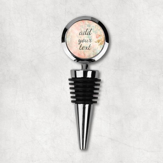 A wine stopper with a metal top and black rubber middle, with a personalised text label that says 'add your text here' on a floral background.