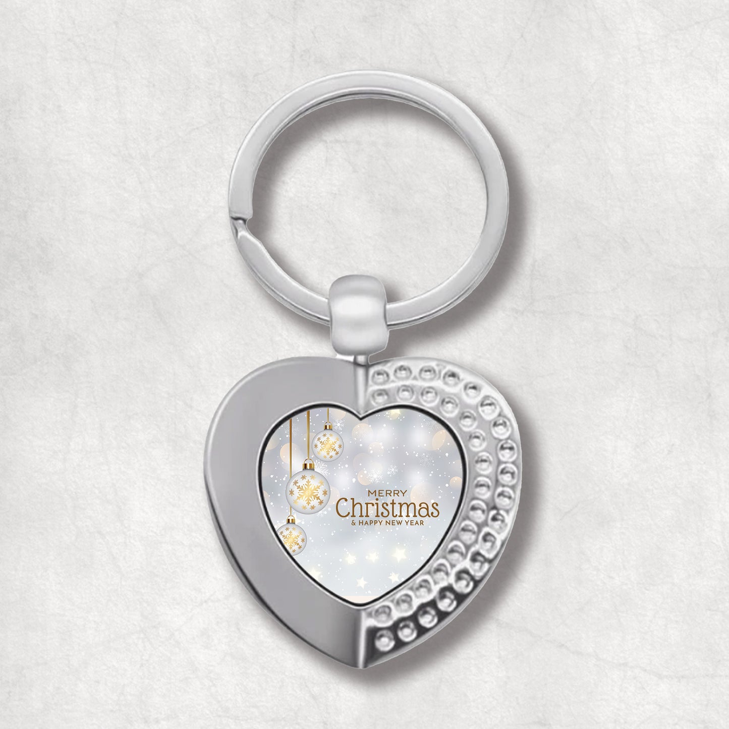 Heart-shaped keyring with Christmas design of snow and white baubles with 'Merry Christmas' text on the light background. An elegant gift for Christmas.