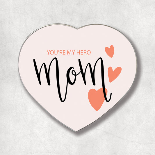 A heart-shaped metal magnet with the text 'YOU'RE MY HERO' and 'mom' in curly black font, accompanied by two pink hearts.