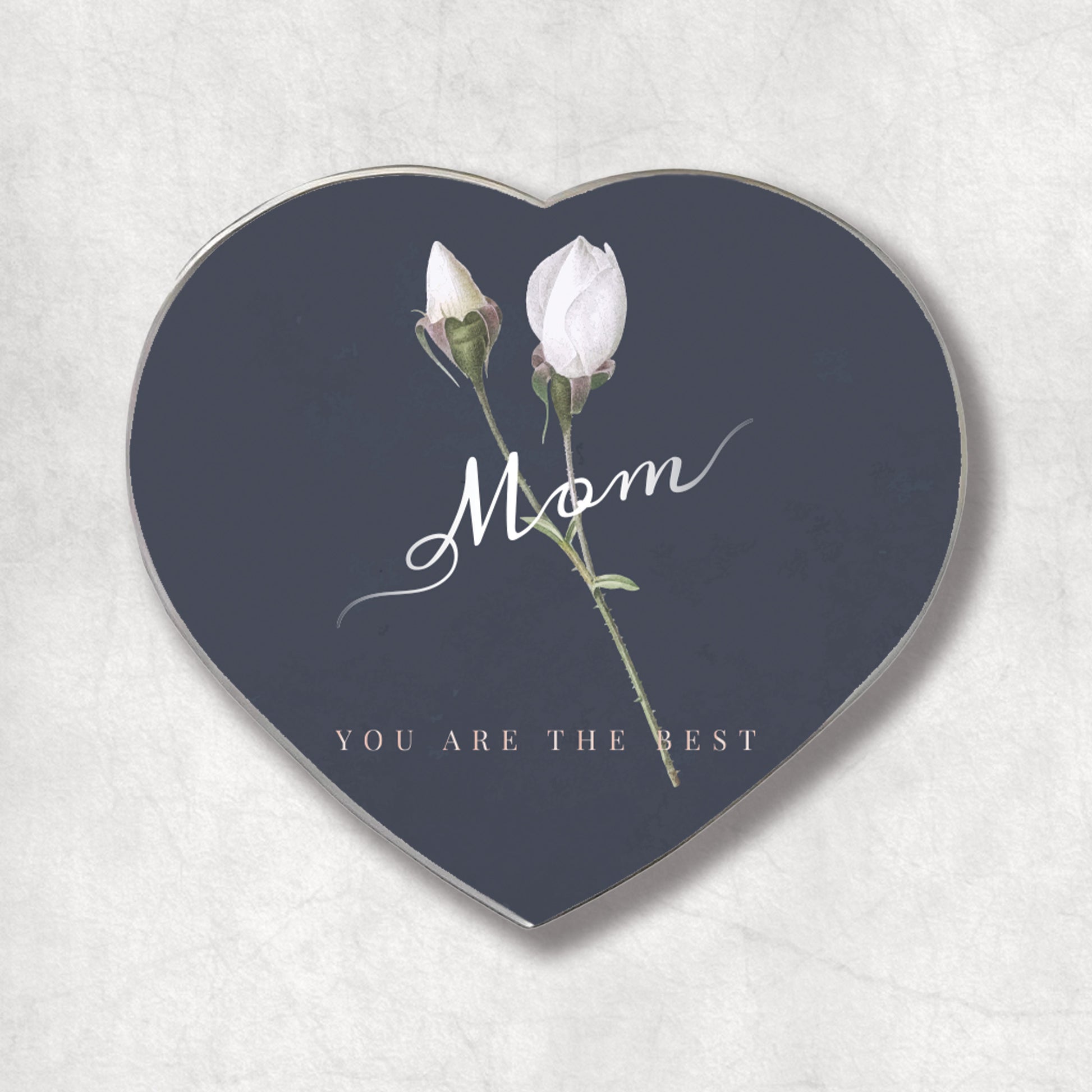 A heart-shaped metal magnet with the 'Mom YOU ARE THE BEST' text on a dark background, accompanied by an image of two white roses.