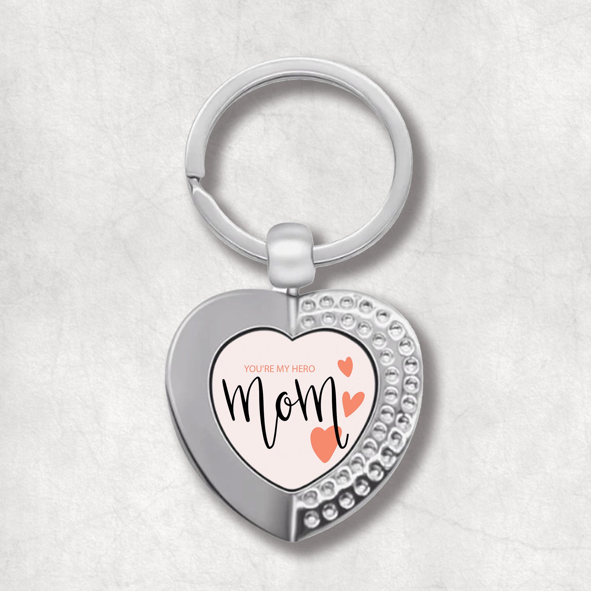 An elegant heart-shaped keyring with a printed message 'Mom You Are My Hero' and three small hearts on the right side.  