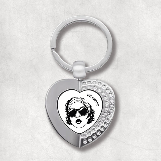 Metal heart-shaped keychain with "Be Proud" text and a woman's face graphic on a white background.