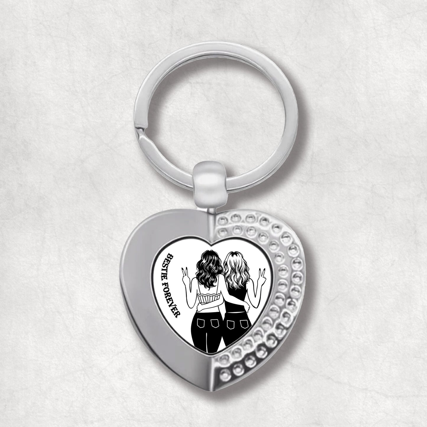 Metal heart-shaped keychain with an illustration of two women and 'Besties Forever' text written on a white background, perfect for celebrating friendship.