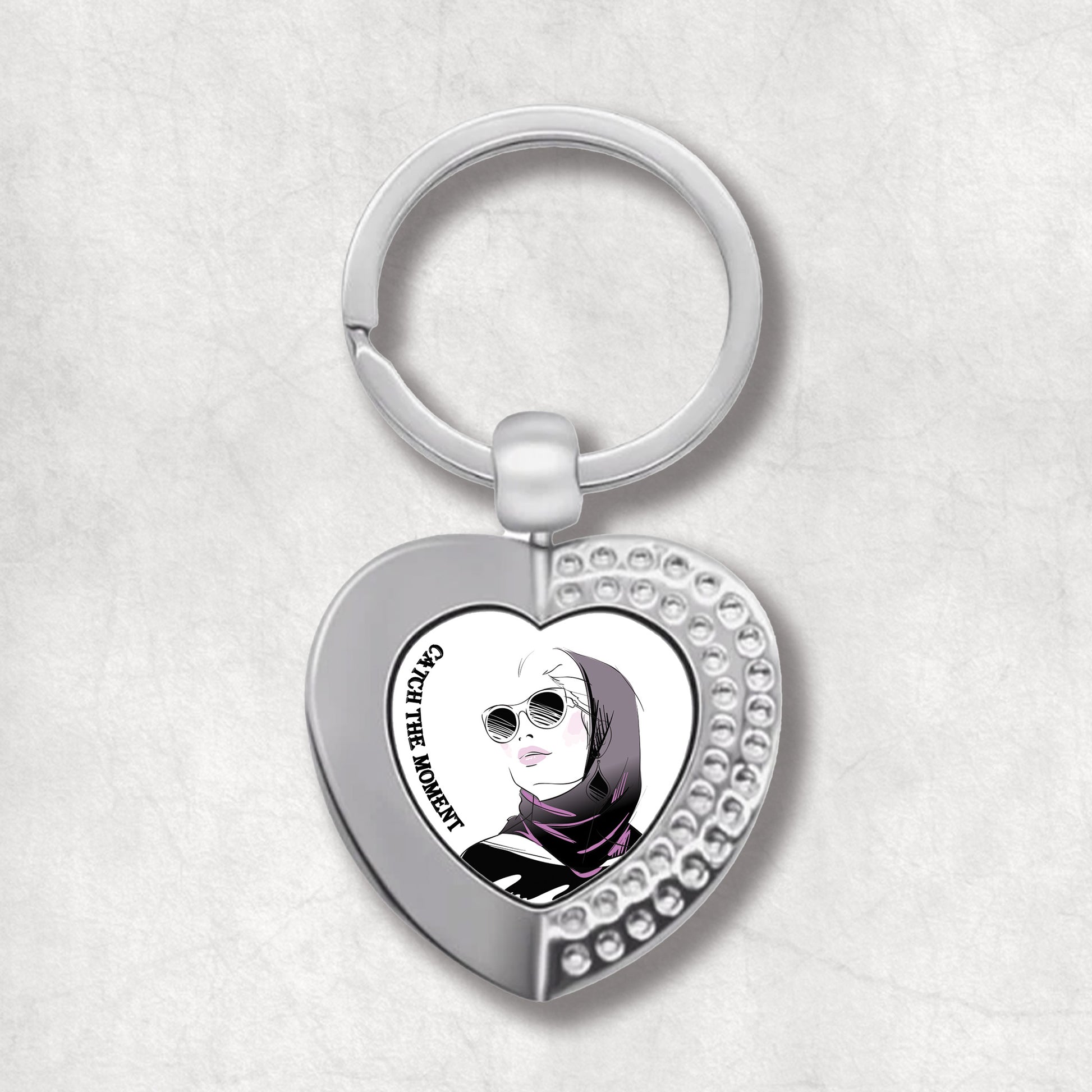 Metal heart-shaped keychain with an image of a woman wearing a hijab and text 'catch the moment' written on a white background.