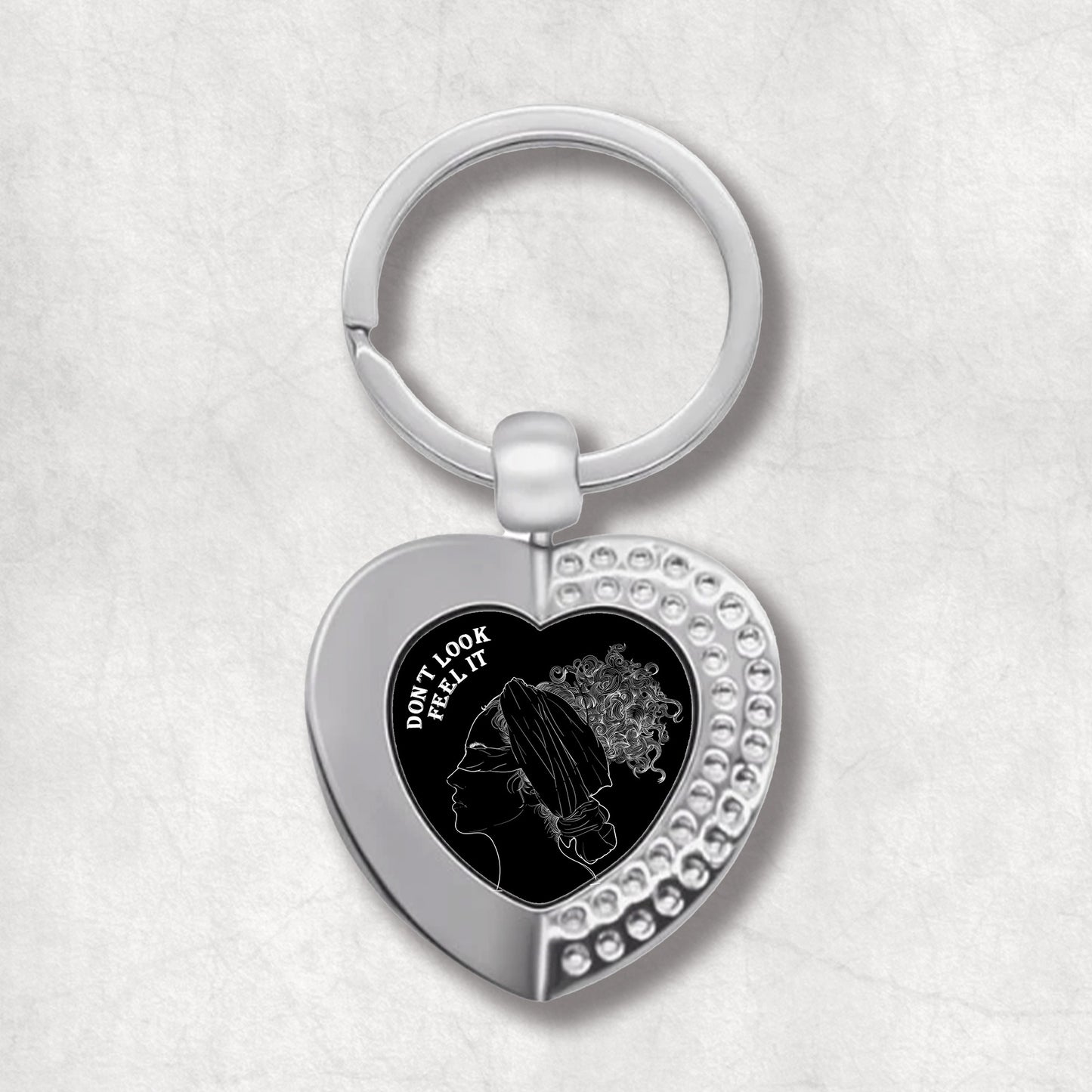 Metal heart-shaped keychain with a woman image and 'Don't Look, Feel It' text written on a black background.