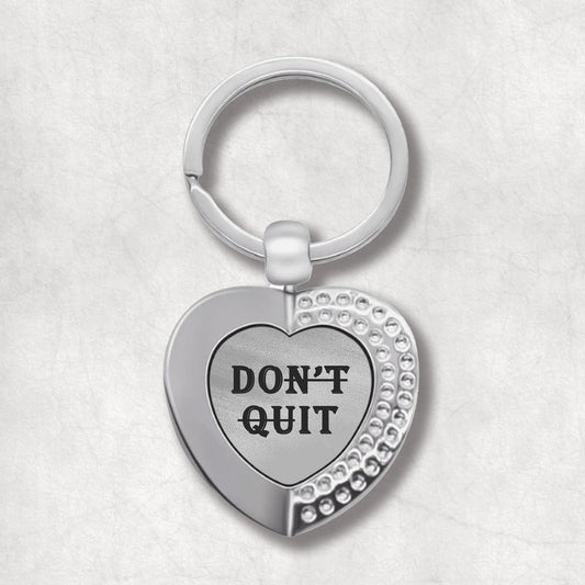 Metal heart-shaped keychain with 'don't quit' text written on a grey patterned background.