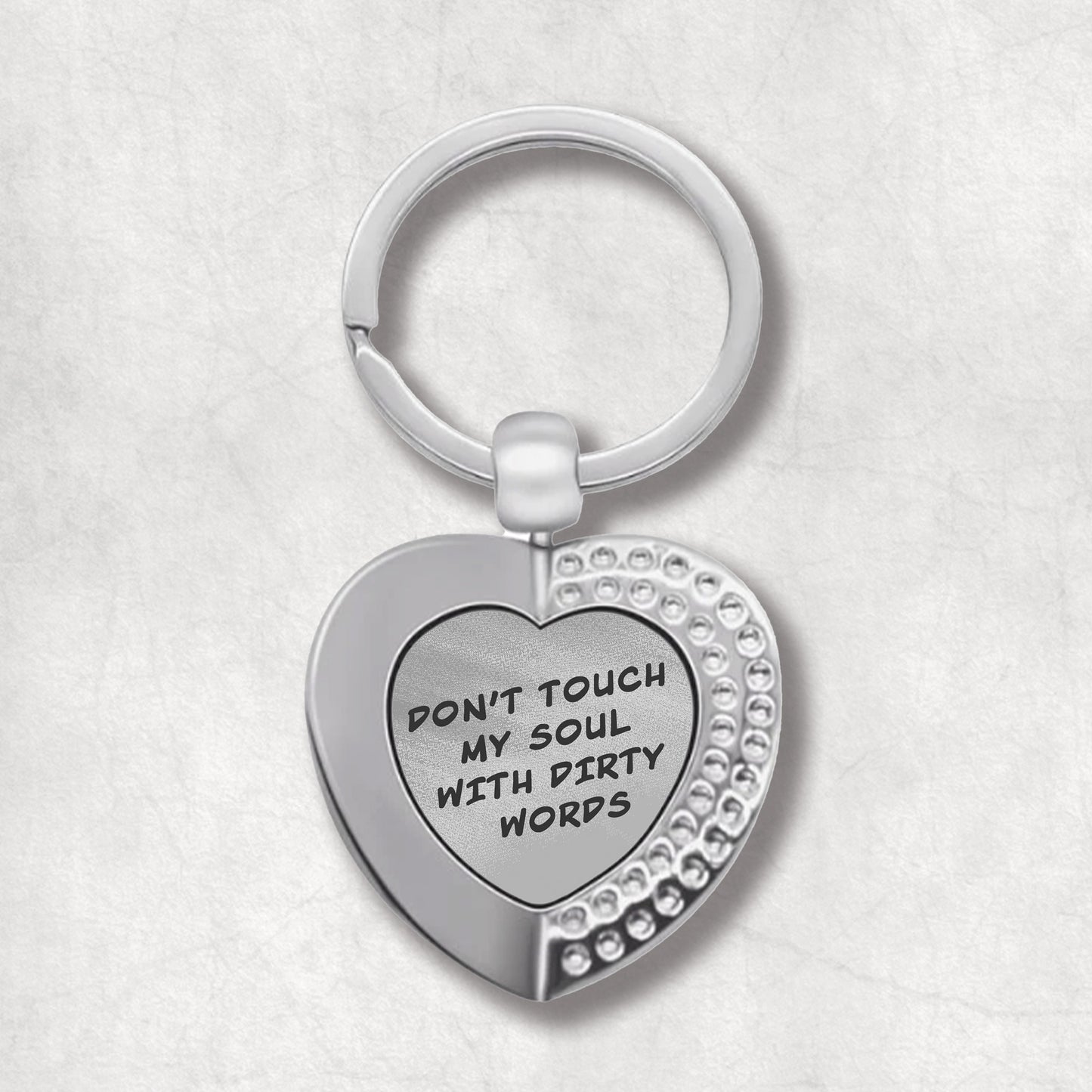 Metal heart-shaped keychain with 'Don't touch my soul with dirty words' text written on a grey patterned background.