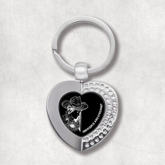 Metal heart-shaped keychain with an image of a woman's face in a hat, flower, and 'Innocence and Forever' text written on a black background.