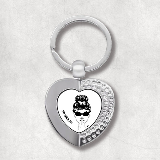 Metal heart-shaped keychain with an illustration of a woman's face, wearing sunglasses, showing middle finger 'so what?' text written on a white background.